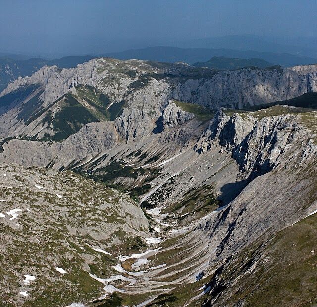 A rugged mountain landscape with steep slopes and patches of snow.