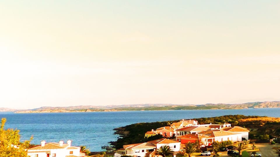 A coastal village with houses near the sea, a clear sky, and distant hills.