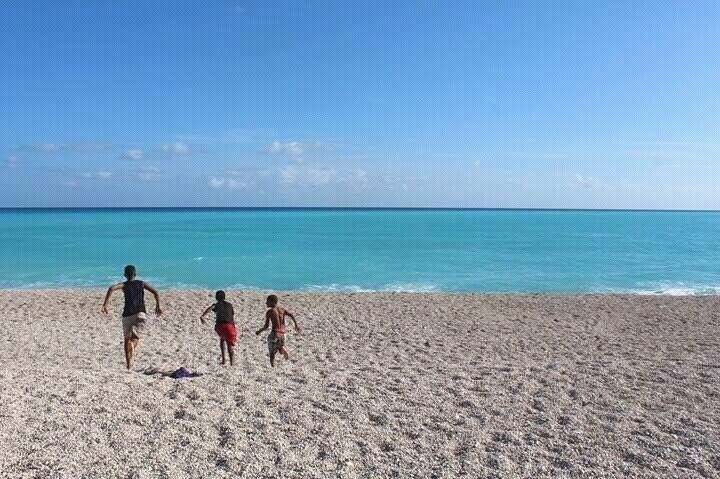 A sandy beach with three people walking towards the ocean.