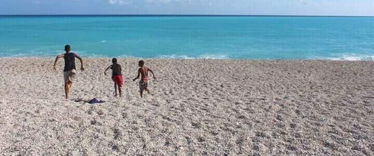 A sandy beach with three people walking towards the ocean.
