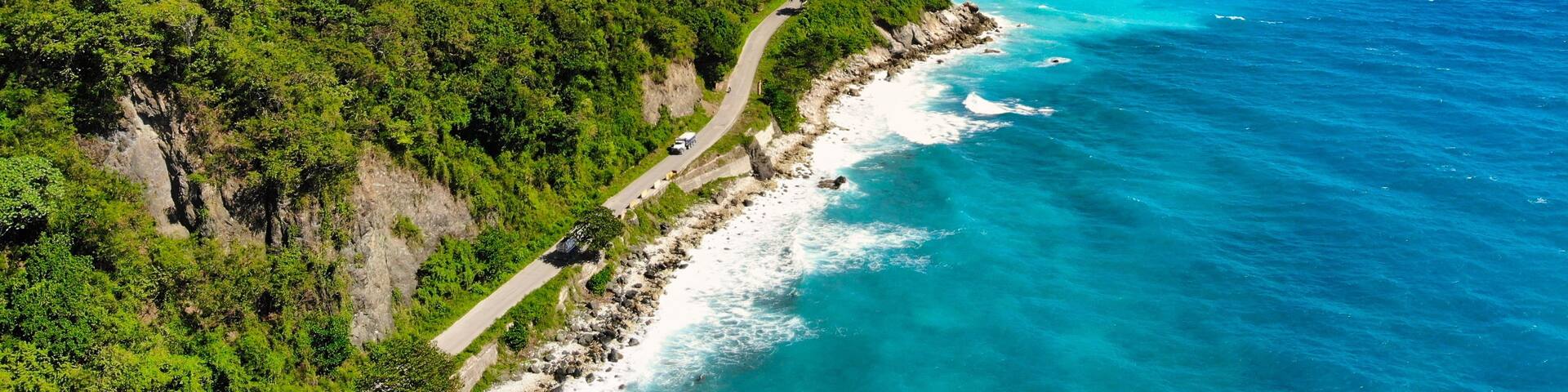 A coastal road winding along a cliffside with turquoise waters and dense greenery.