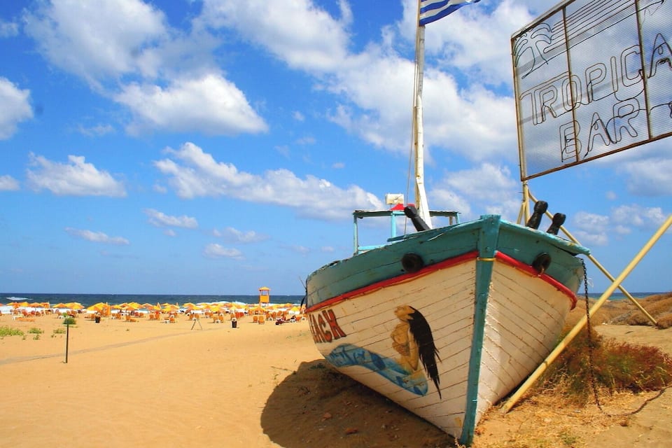 A beach with a boat, umbrellas, and a sign reading "TROPICA BAR".