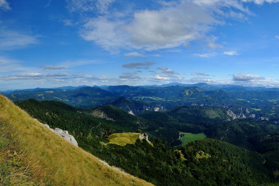Ein weitreichender Panoramablick auf eine Berglandschaft mit einem See und bewaldeten Tälern.