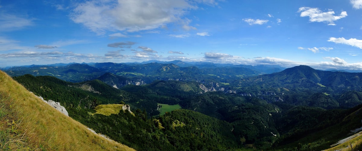 A panoramic view of a mountainous landscape with a lake and forested valleys.