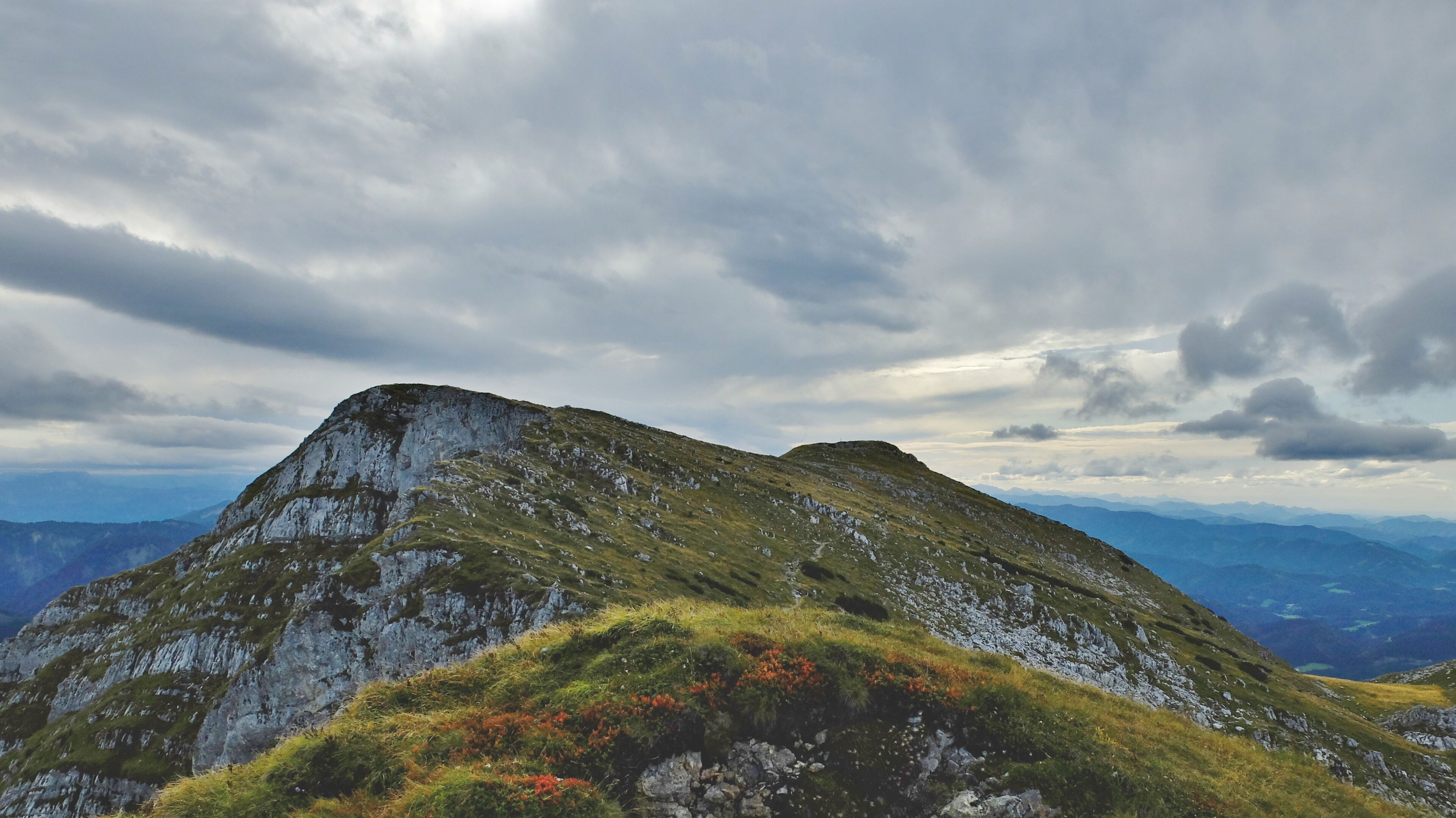 A mountain with a grassy peak and rocky slopes under a cloudy sky.