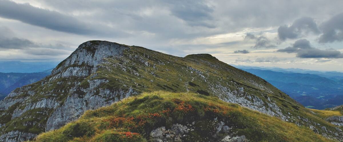 A mountain with a grassy peak and rocky slopes under a cloudy sky.