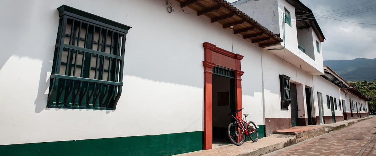 A white building with green trim and a red door, a bicycle parked in front, and a brick-paved street.