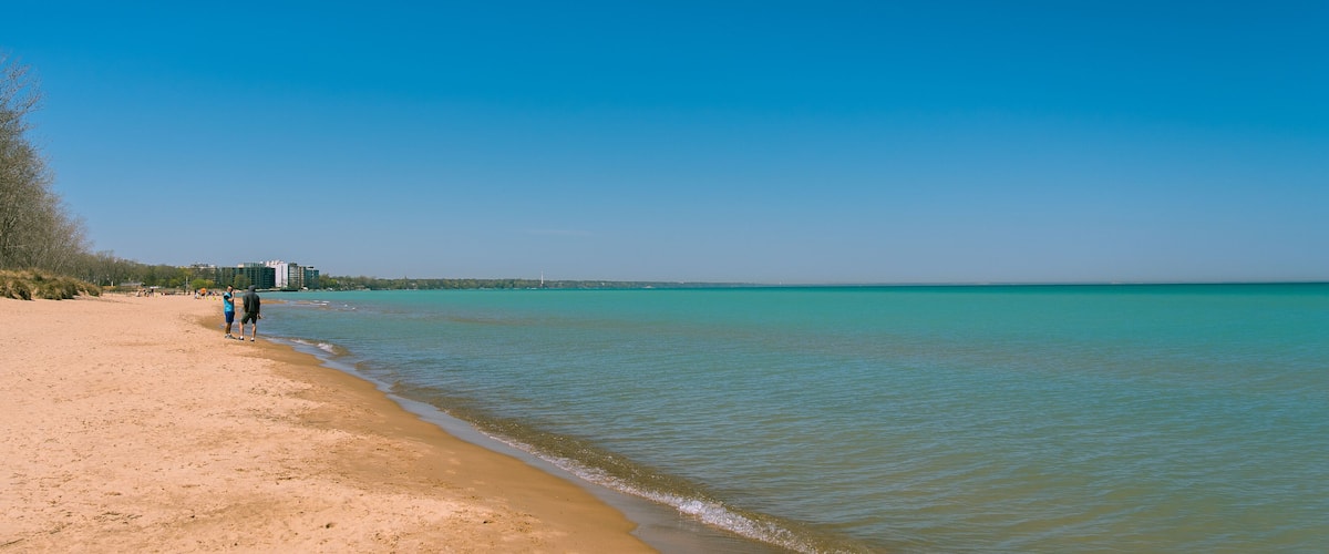 A beach with clear turquoise water, a sandy shore, and a few people walking along the beach.