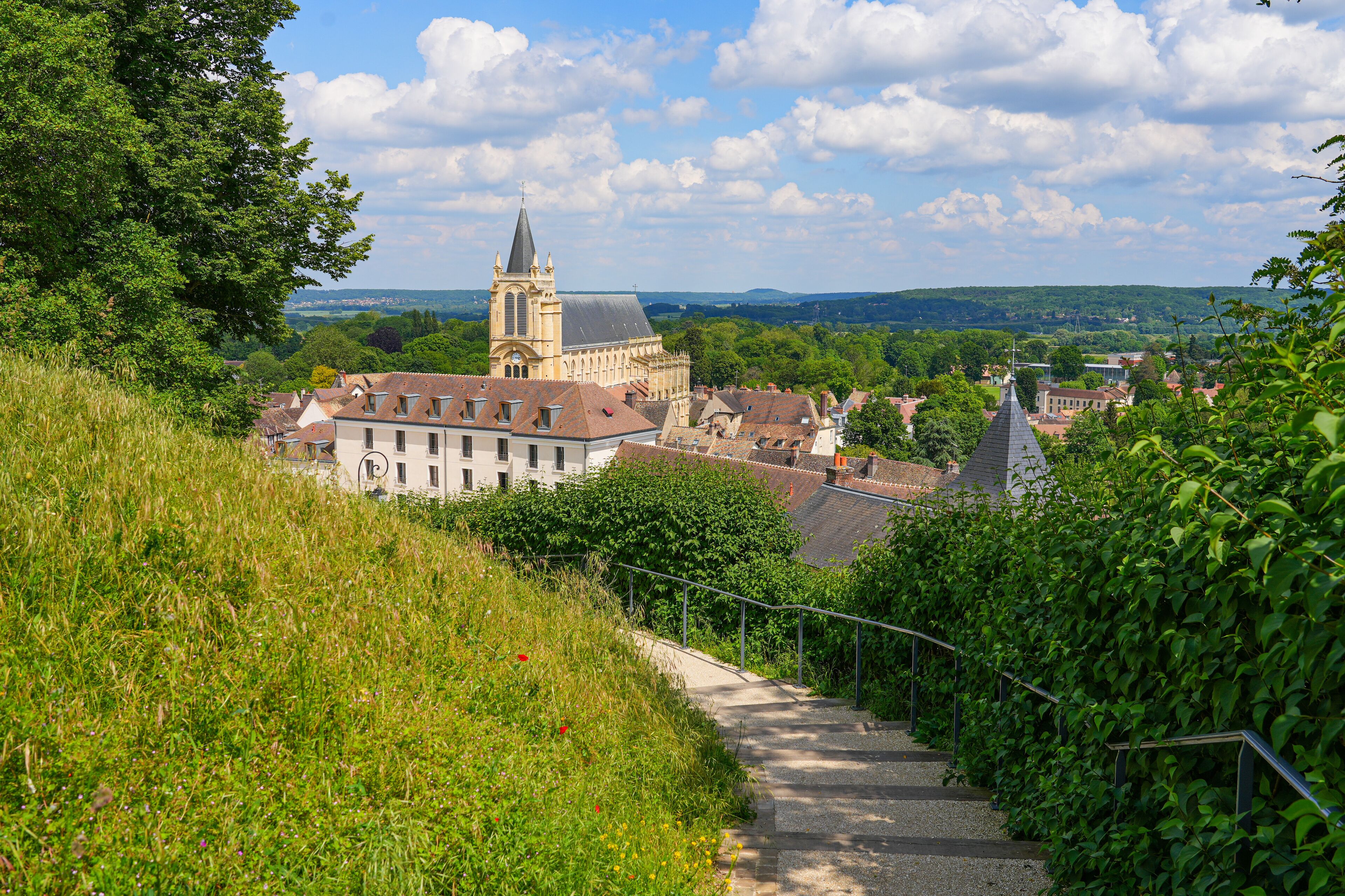 A town with a prominent church tower, lush greenery, and a hillside path.