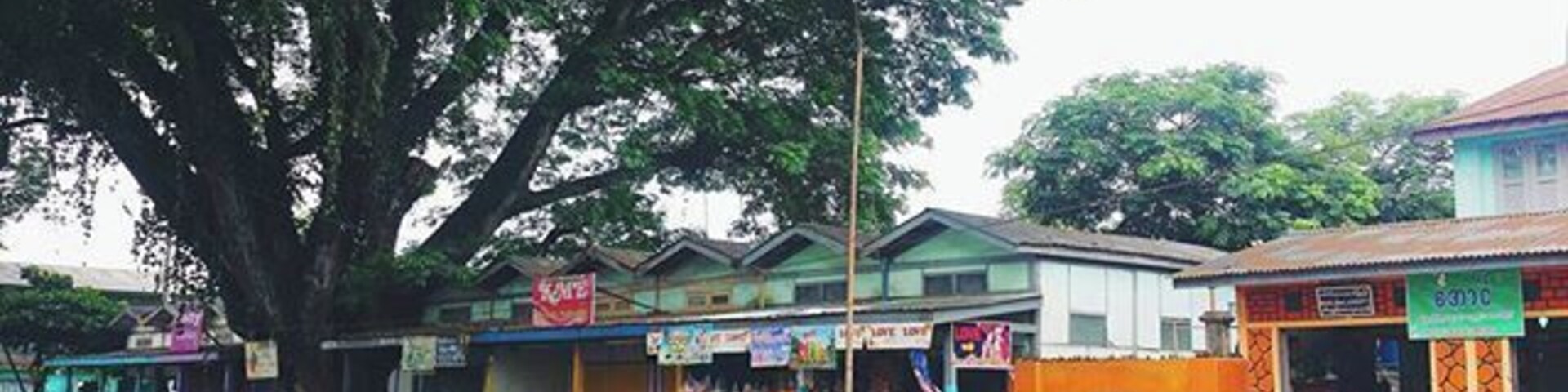 Una calle con un árbol grande, tiendas y dos personas vestidas con trajes tradicionales.