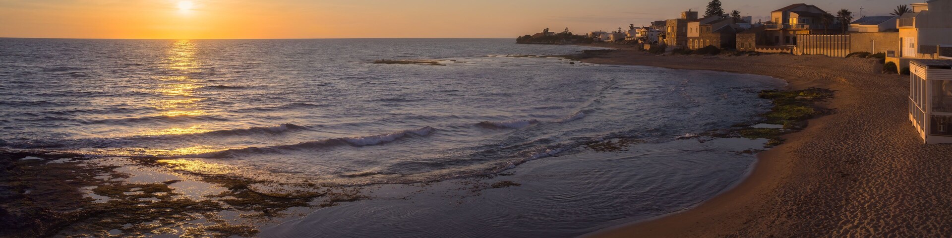 Una playa con olas, un atardecer y edificios a lo largo de la costa.