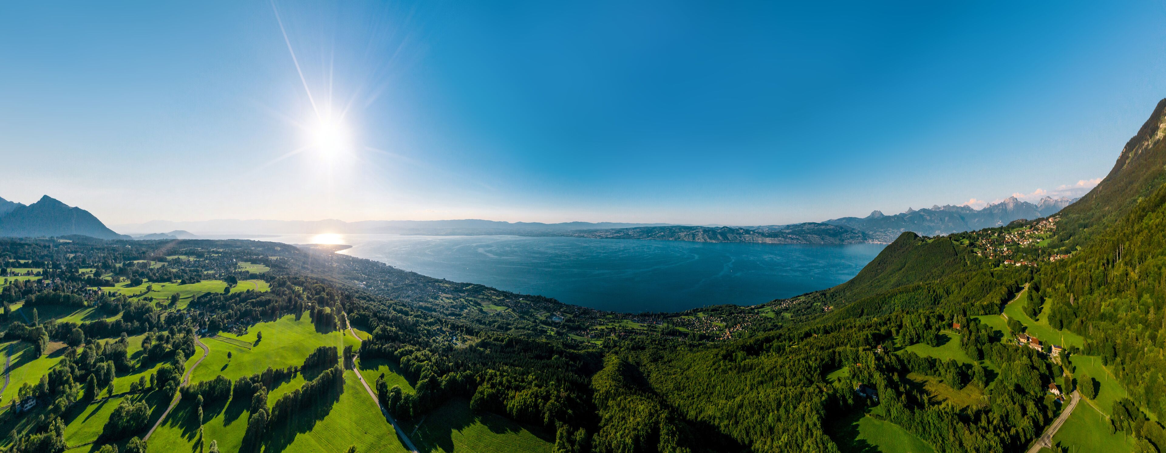 A mountainous landscape with a lake, green fields, and a clear sky.