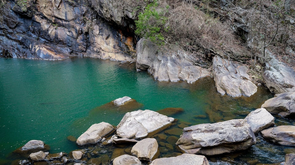 A clear turquoise river with large rocks in the foreground and rocky cliffs in the background.