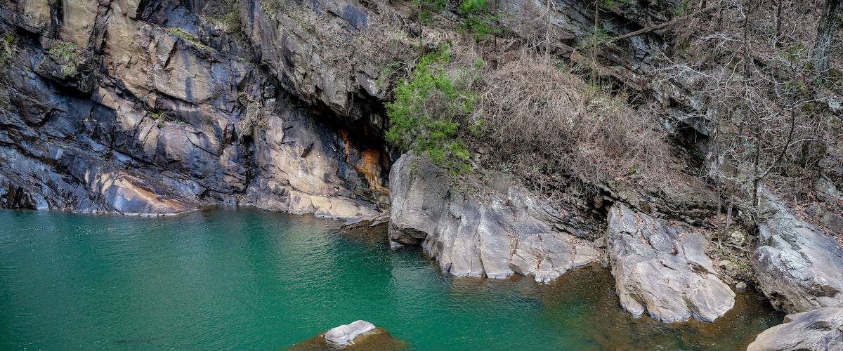 A clear turquoise river with large rocks in the foreground and rocky cliffs in the background.