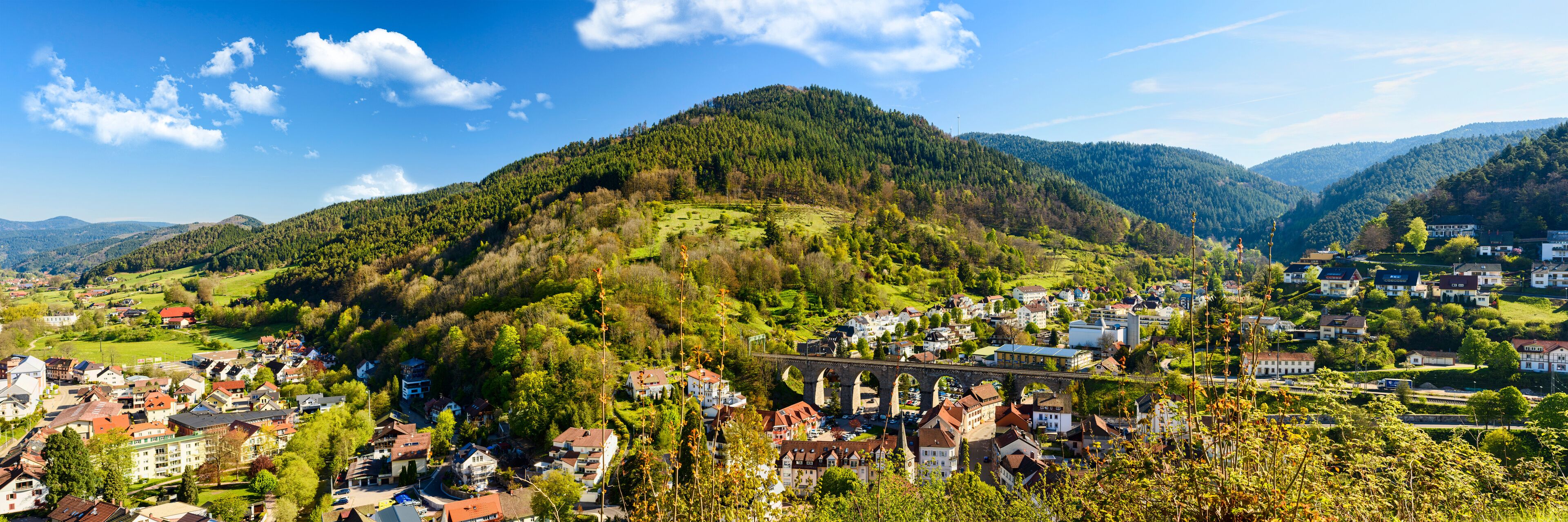 A town nestled in a valley with a prominent bridge and lush green hills in the background.