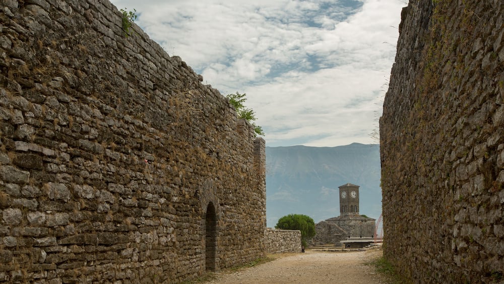 A stone pathway flanked by ancient walls leading to a tower with a clock.