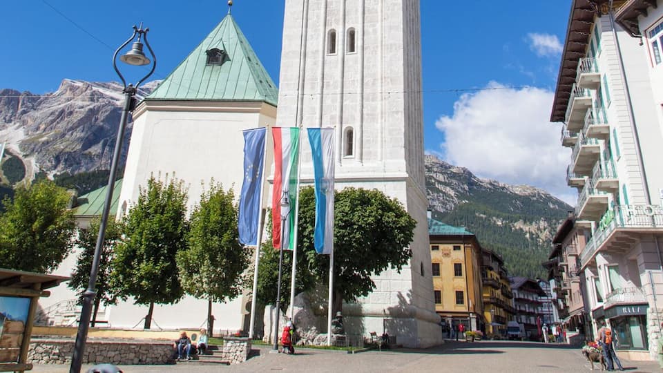 A tall white tower with a clock, surrounded by buildings and mountains.