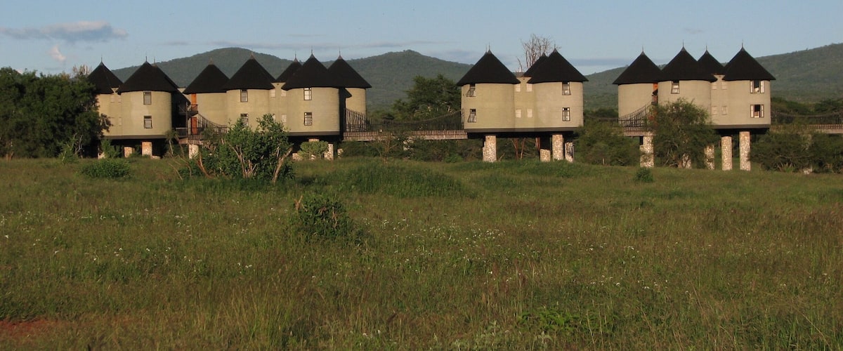 A row of castle-like buildings with conical roofs in a grassy field.