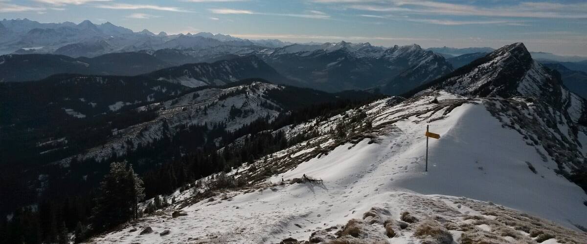 A snow-covered mountain peak with a trail and a signpost.