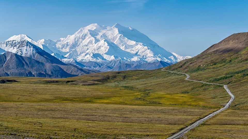 A snow-capped mountain range with a winding road leading towards it.