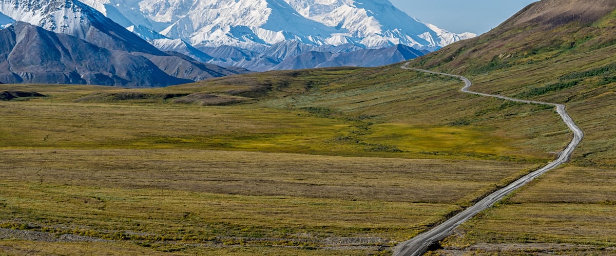 A snow-capped mountain range with a winding road leading towards it.