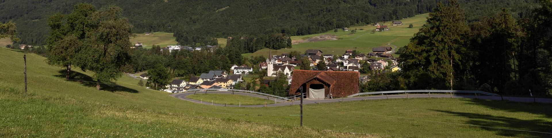 A mountain with a small village at its base, surrounded by lush greenery and a clear sky.