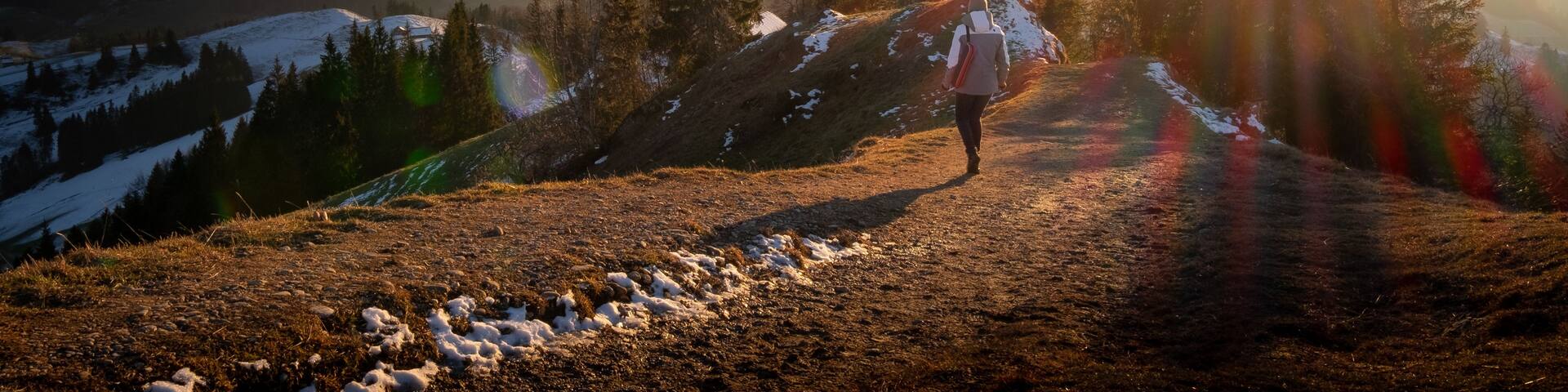 A hiker on a snow-covered mountain path with a sunrise in the background.