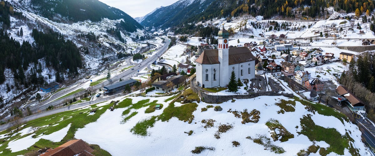 Un pueblo cubierto de nieve en la montaña, con una iglesia destacada, carreteras sinuosas y un valle.
