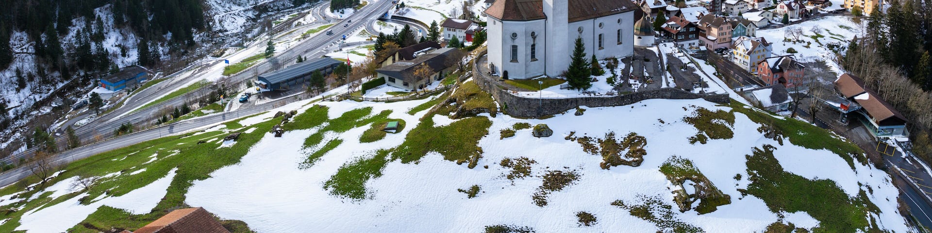 A snow-covered mountain town with a prominent church, winding roads, and a valley.