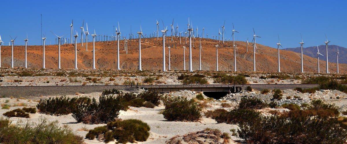 A desert landscape with wind turbines and a bridge.