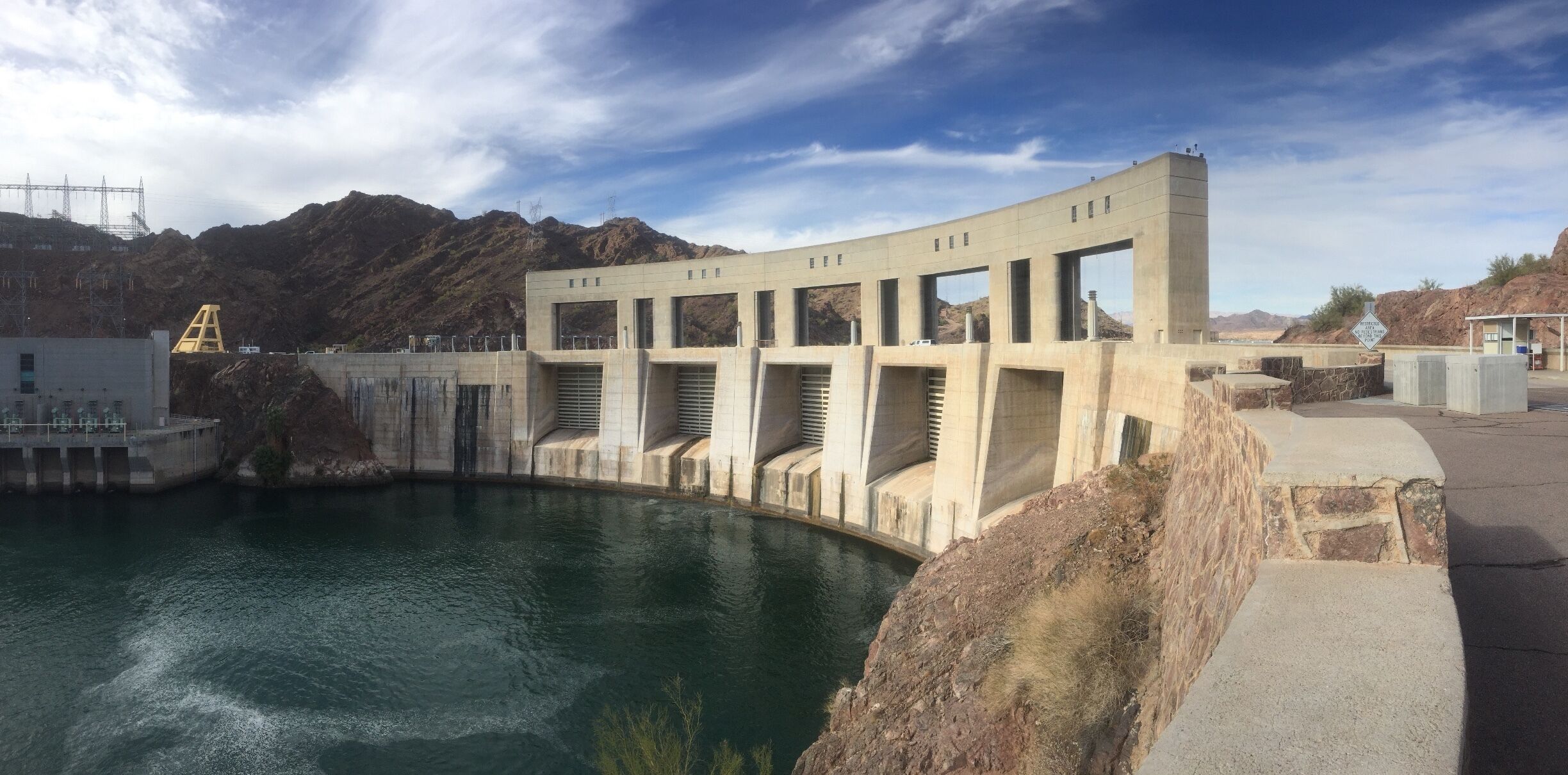 A dam with a reservoir, mountains in the background, and a clear sky.