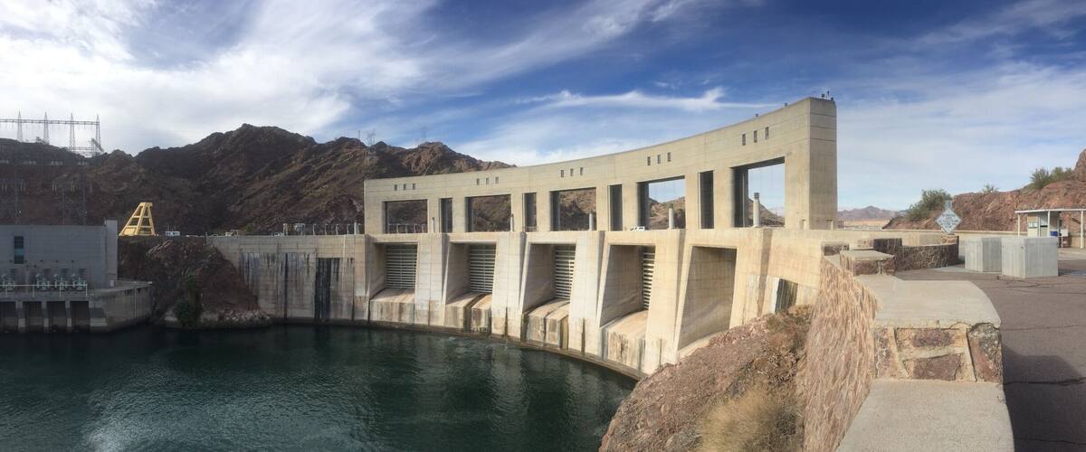 A dam with a reservoir, mountains in the background, and a clear sky.
