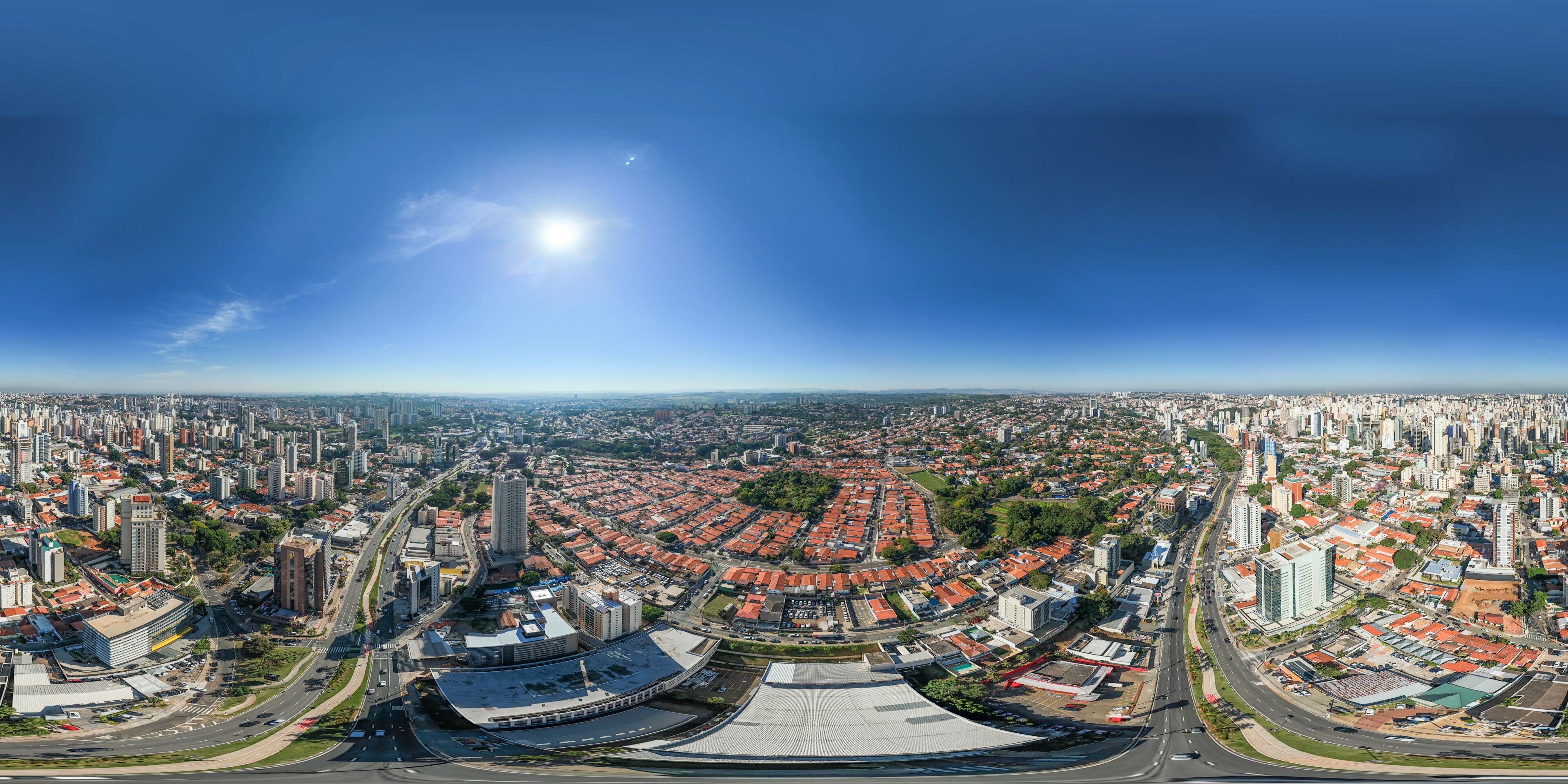 A panoramic cityscape with a prominent stadium, dense urban buildings, and a clear blue sky.