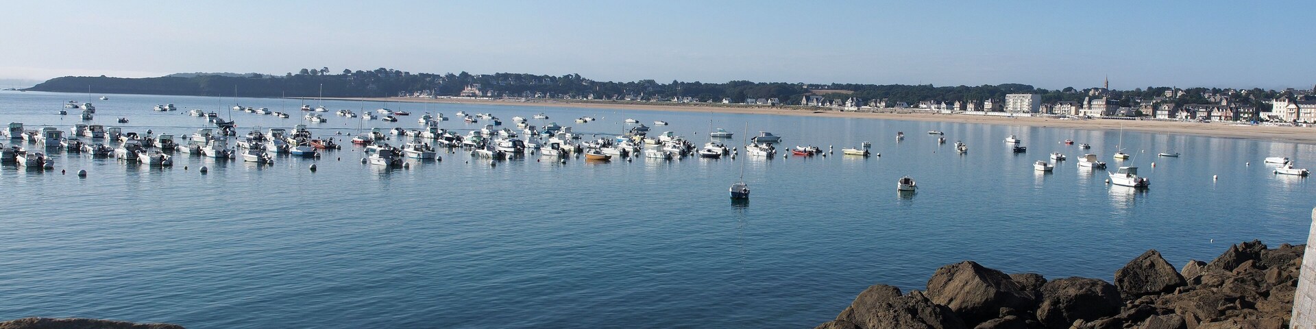 A rocky shoreline with numerous boats anchored in calm waters.