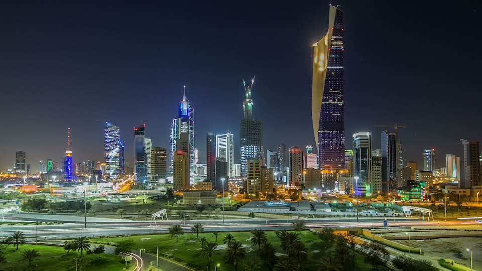 A city skyline at night with illuminated buildings and a highway in the foreground.