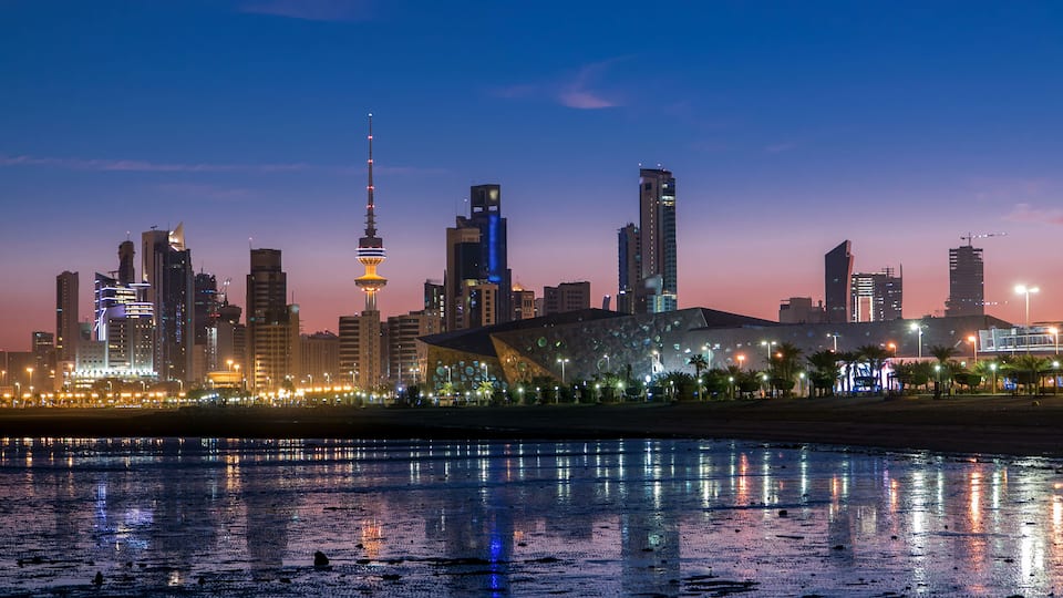 A city skyline at dusk with illuminated buildings and a prominent tower.