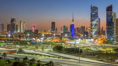 A city skyline at dusk with illuminated buildings and a prominent tower.
