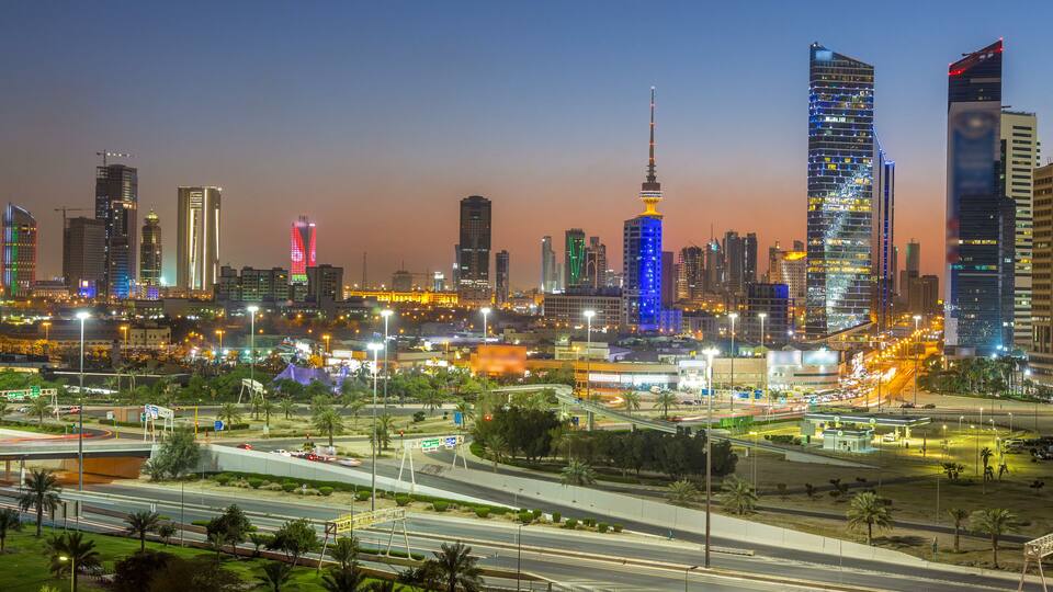 A city skyline at dusk with illuminated buildings and a prominent tower.