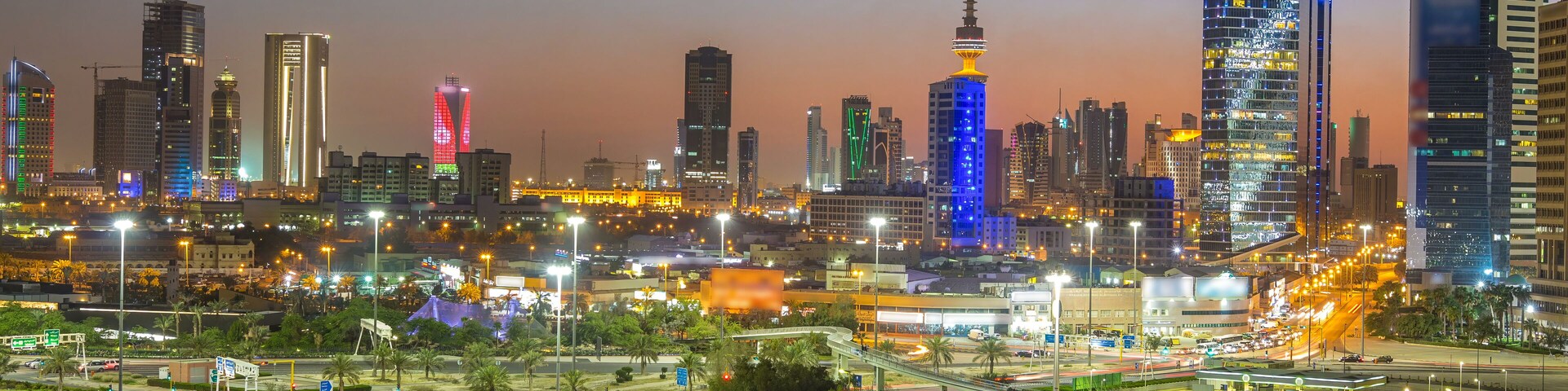 A city skyline at dusk with illuminated buildings and a prominent tower.