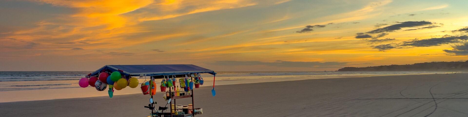 Una playa con un carrito y globos, un atardecer y cielo despejado.
