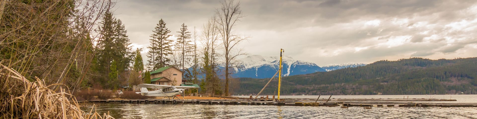 A lake with a small house and a dock, surrounded by trees and mountains in the background.