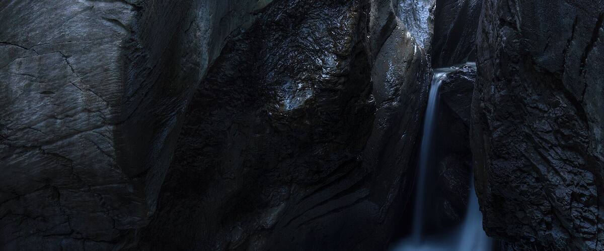 A narrow, rocky canyon with a waterfall.