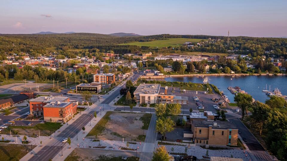 A riverside town with a marina, buildings, and a hilly backdrop.