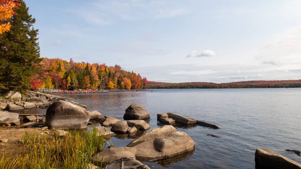 A lake surrounded by autumn-colored trees, large rocks in the foreground, and a distant view of a bridge.