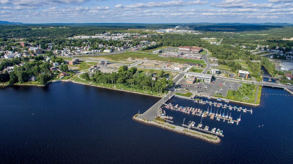 An aerial view of a town with a marina, industrial buildings, and surrounding greenery.