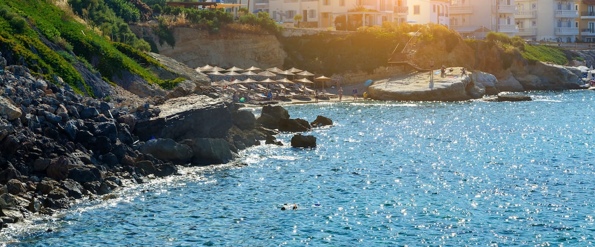 A coastal town with buildings, rocky shoreline, and clear blue sea.