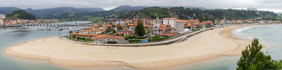 A coastal town with a sandy beach, a marina with boats, and buildings with red roofs.