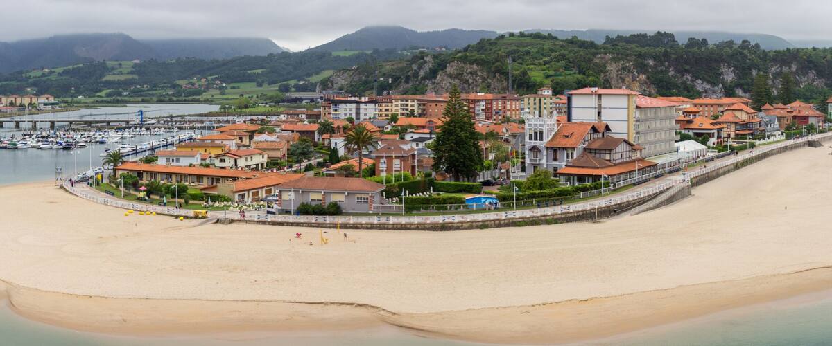 A coastal town with a sandy beach, a marina with boats, and buildings with red roofs.