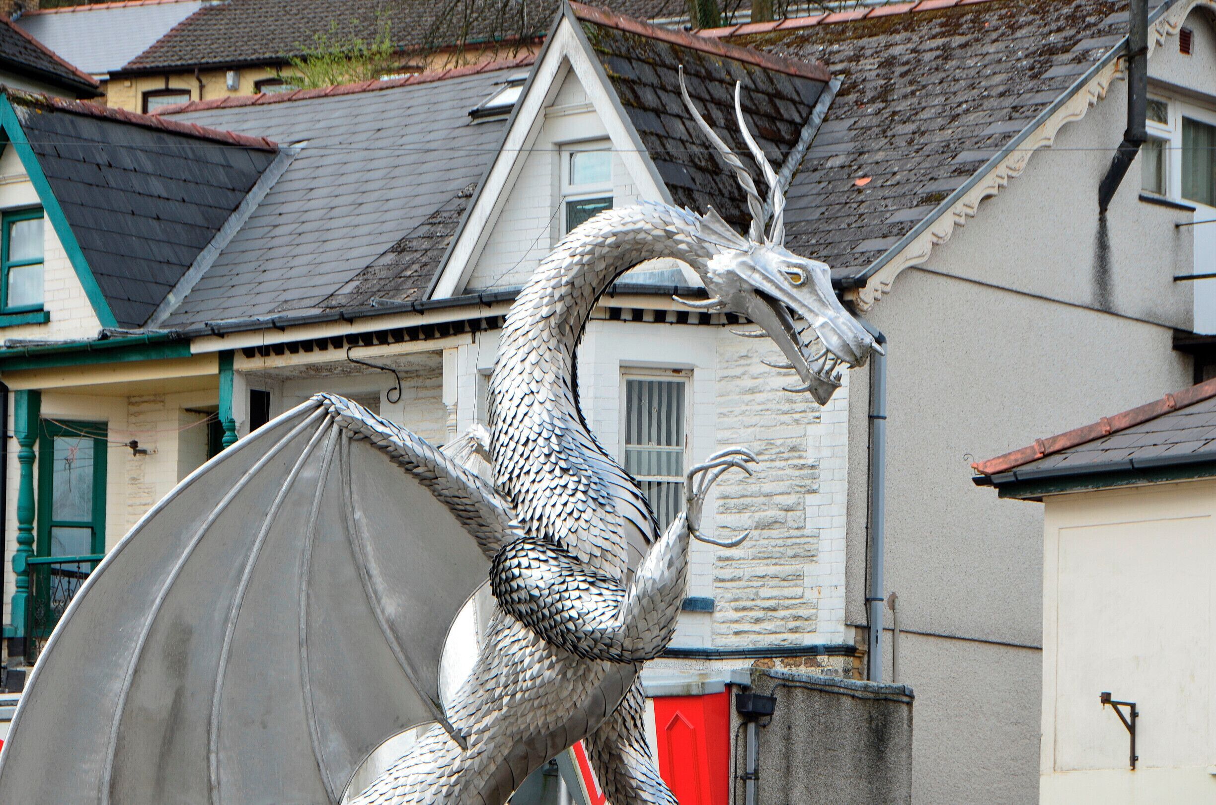 Une statue de dragon sur une place publique, avec des maisons en arrière-plan.
