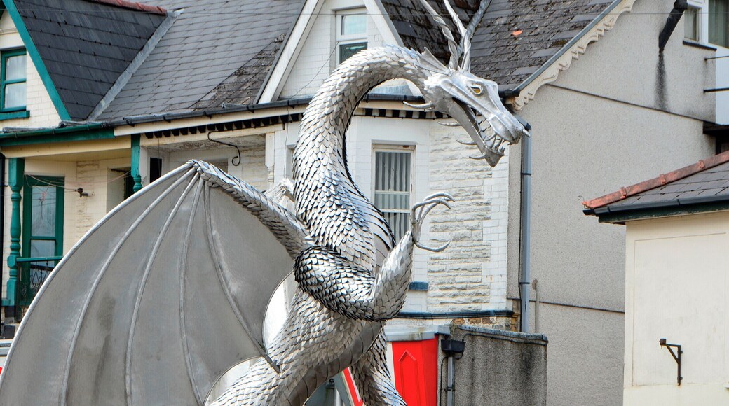 Une statue de dragon sur une place publique, avec des maisons en arrière-plan.